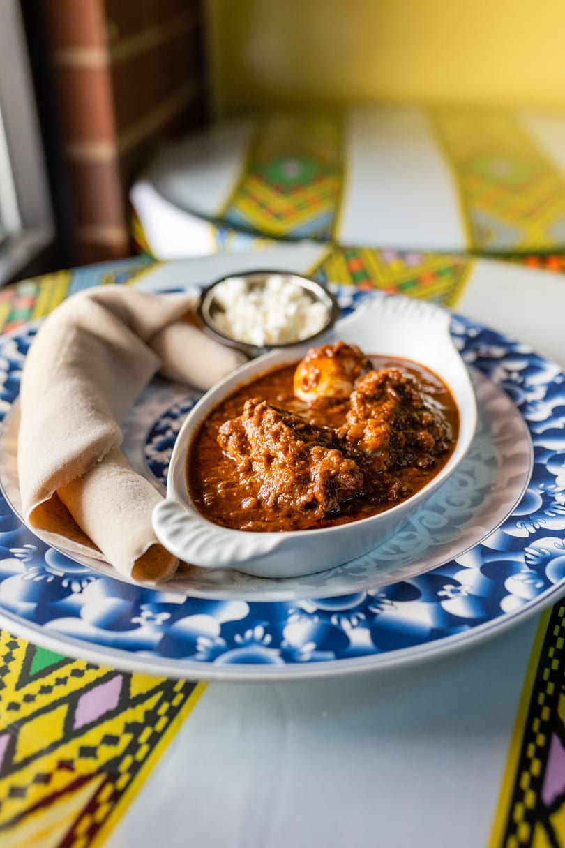 Doro Wat, an Ethiopian chicken stew, with injera bread and a side of cheese on a blue patterned plate.