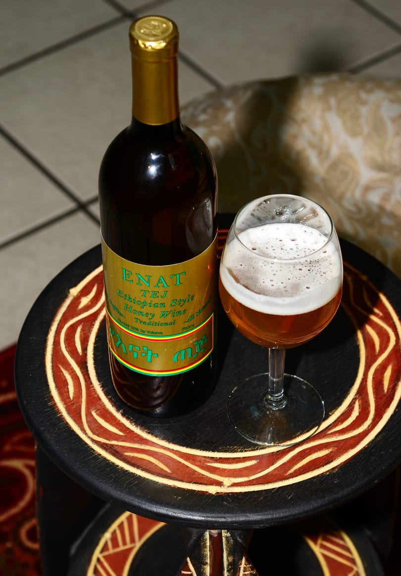 A bottle of Enat Tej Ethiopian honey wine and a glass of the amber-colored wine with foam.