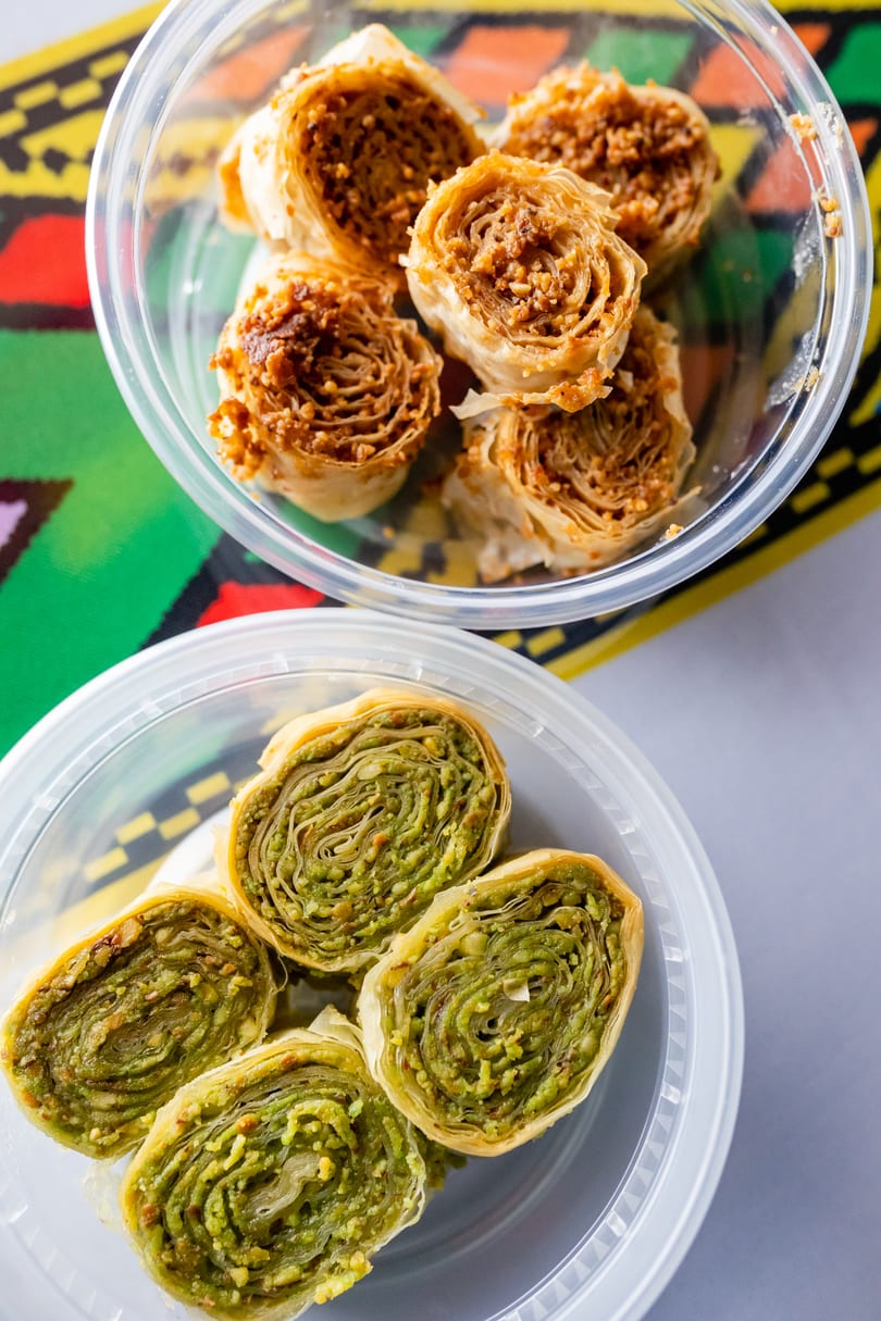 Two plastic containers of rolled baklava, one with pistachio and one with walnuts.