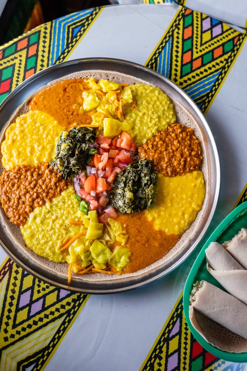 A large platter of colorful Ethiopian food, including injera, stews, and vegetables, on a patterned tablecloth.